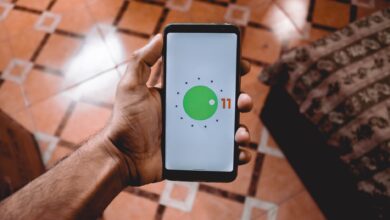 Close-up of a hand holding a smartphone displaying Android 11 interface indoors on patterned floor.