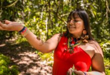 Smiling woman in traditional Amazonian outfit interacting with nature in a lush forest.