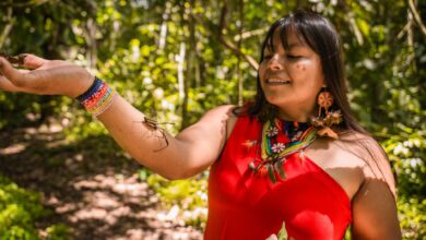 Smiling woman in traditional Amazonian outfit interacting with nature in a lush forest.