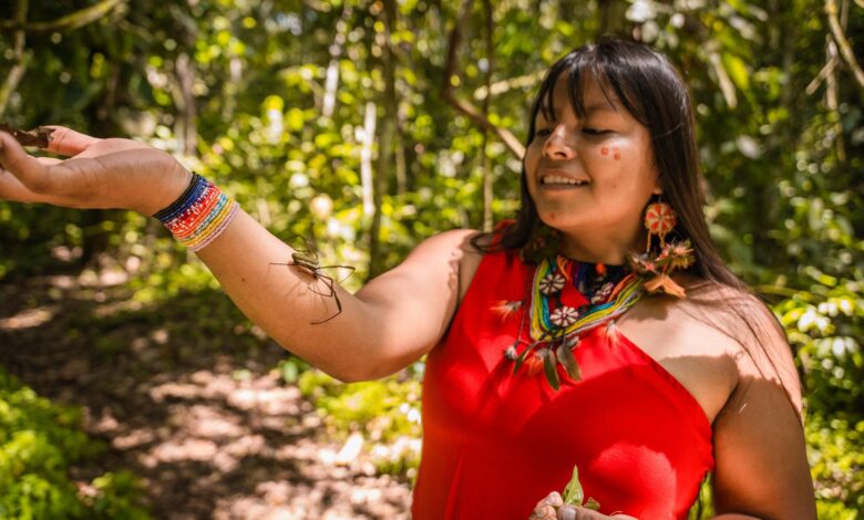 Smiling woman in traditional Amazonian outfit interacting with nature in a lush forest.