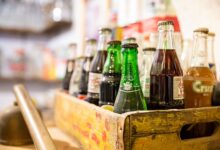 A collection of assorted vintage soda bottles in a rustic wooden crate with blurred background.