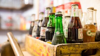 A collection of assorted vintage soda bottles in a rustic wooden crate with blurred background.