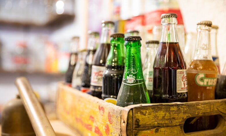 A collection of assorted vintage soda bottles in a rustic wooden crate with blurred background.