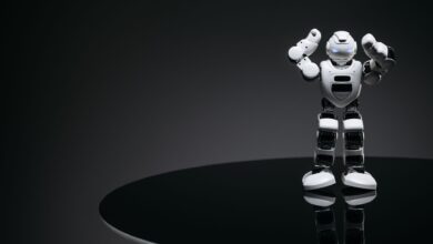 A small humanoid robot with glowing eyes on a reflective table in a dark setting.