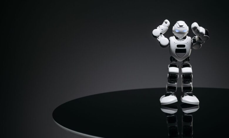A small humanoid robot with glowing eyes on a reflective table in a dark setting.