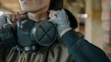 A person with a gas mask and bandaged hands in an urban setting, indicating survival theme.