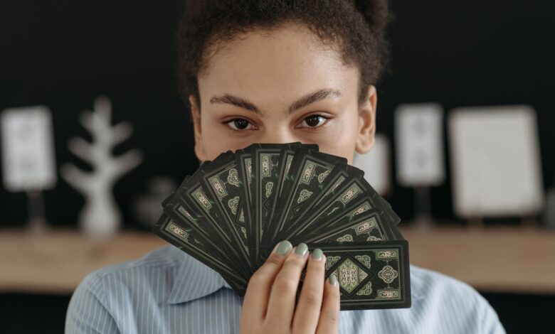 A woman with a focused expression holding a fan of tarot cards, conveying mystery and reflection.