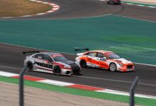 Two racecars compete at high speed on a professional race track, showcasing thrilling motorsport action.