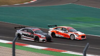 Two racecars compete at high speed on a professional race track, showcasing thrilling motorsport action.