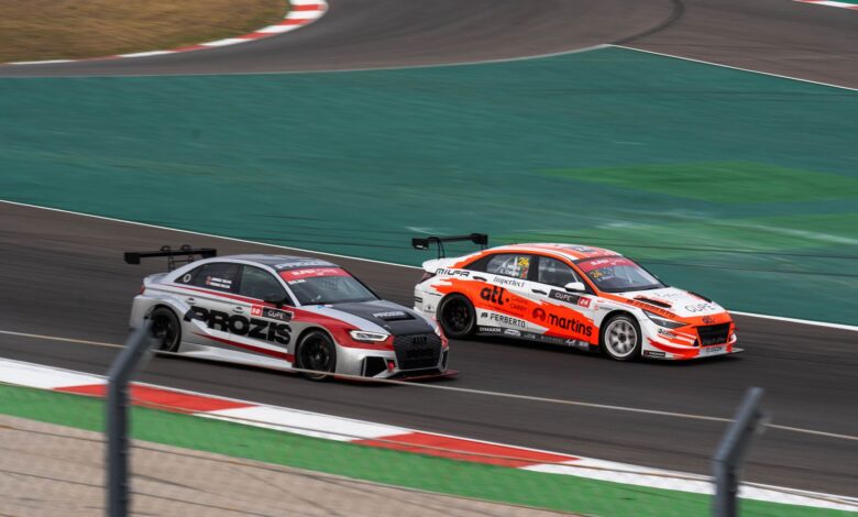 Two racecars compete at high speed on a professional race track, showcasing thrilling motorsport action.