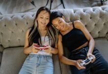 Two women relaxing and playing video games on a comfortable sofa together.