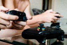 Two people playing video games with controllers on a glass table indoors.