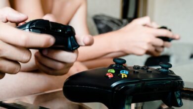 Two people playing video games with controllers on a glass table indoors.