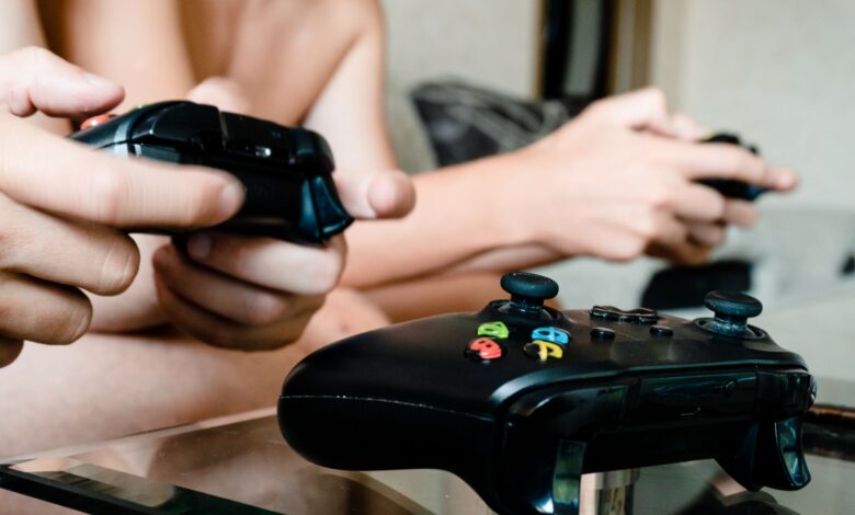 Two people playing video games with controllers on a glass table indoors.