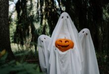 Three ghostly figures holding a carved pumpkin in a mysterious forest setting, perfect for Halloween imagery.
