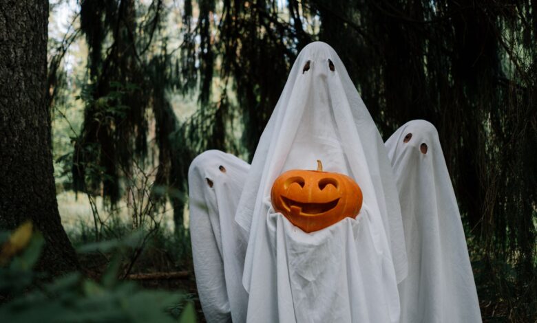 Three ghostly figures holding a carved pumpkin in a mysterious forest setting, perfect for Halloween imagery.