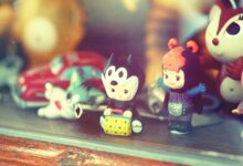 Close-up of vintage toy figurines on a wooden shelf inside a glass display case.