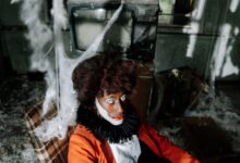 Creepy clown in an abandoned room filled with cobwebs, creating a spooky Halloween ambiance.