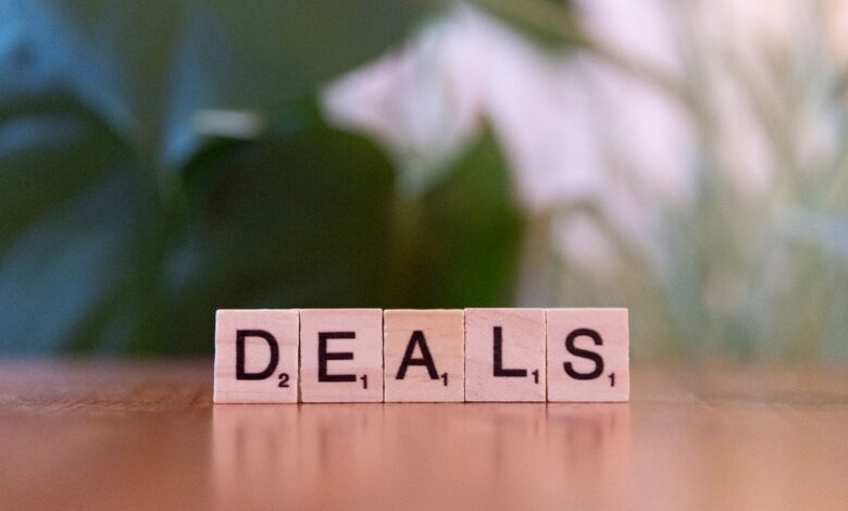 Close-up of Scrabble tiles spelling 'DEALS' on a wooden surface with blurry green background.