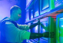 Man with prosthetic arms interacting with stack of CRT televisions, showcasing technology.