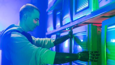 Man with prosthetic arms interacting with stack of CRT televisions, showcasing technology.