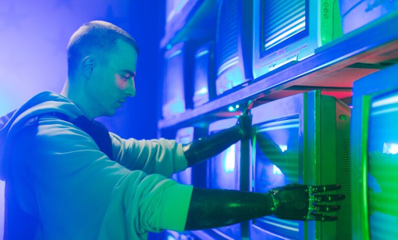 Man with prosthetic arms interacting with stack of CRT televisions, showcasing technology.