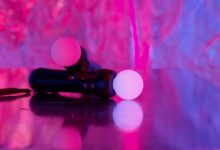 Close-up of neon-lit gaming controllers on a reflective surface, highlighting vibrant colors and modern technology.
