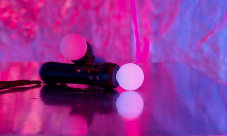 Close-up of neon-lit gaming controllers on a reflective surface, highlighting vibrant colors and modern technology.