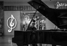 Black and white image of a man playing a grand piano indoors with musical symbols in the background.