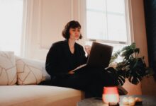 Woman in suit using laptop on sofa in bright room, modern lifestyle.