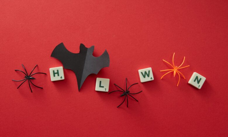 Festive Halloween flat lay with toy spiders, letters, and bat cutout on red background.
