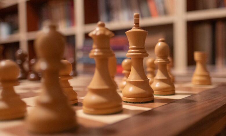 Close-up of wooden chess pieces on a chessboard in a warm, cozy library setting.