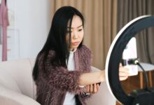 An Asian woman vlogs at home using a smartphone and ring light, perfect setup for influencers.