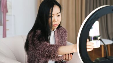 An Asian woman vlogs at home using a smartphone and ring light, perfect setup for influencers.