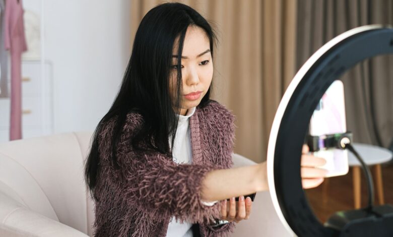 An Asian woman vlogs at home using a smartphone and ring light, perfect setup for influencers.