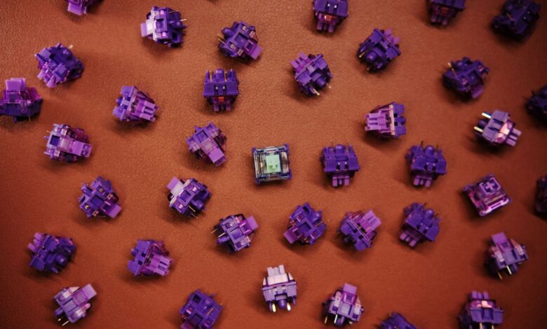 Flat lay of purple mechanical keyboard switches scattered on a brown surface.
