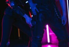 Two people in dark, neon-lit room holding weapons, creating a dramatic scene.