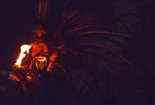 A person in a feathered headdress holding fire in the dark, evoking mystery and intrigue.