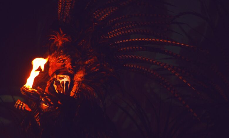 A person in a feathered headdress holding fire in the dark, evoking mystery and intrigue.