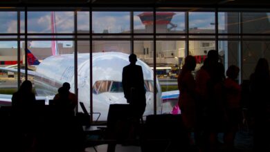Silhouettes of travelers waiting at an airport terminal with an airplane visible through the window.