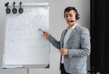 Asian man in a gray suit giving a presentation with a flipchart, wearing a headset.