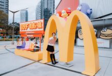 Fashion model poses at McDonald's landmark in vibrant urban setting.