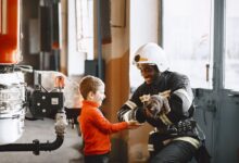 A firefighter handing a rescued cat to a smiling child indoors.