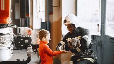 A firefighter handing a rescued cat to a smiling child indoors.