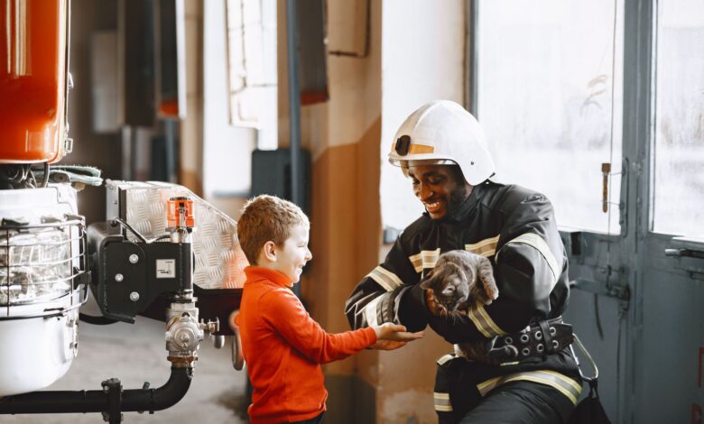 A firefighter handing a rescued cat to a smiling child indoors.