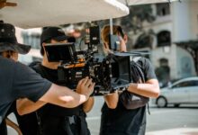 A film crew operates a RED camera on a city street, capturing a professional scene.