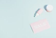 Pink beauty products and sale sign on pastel backdrop.