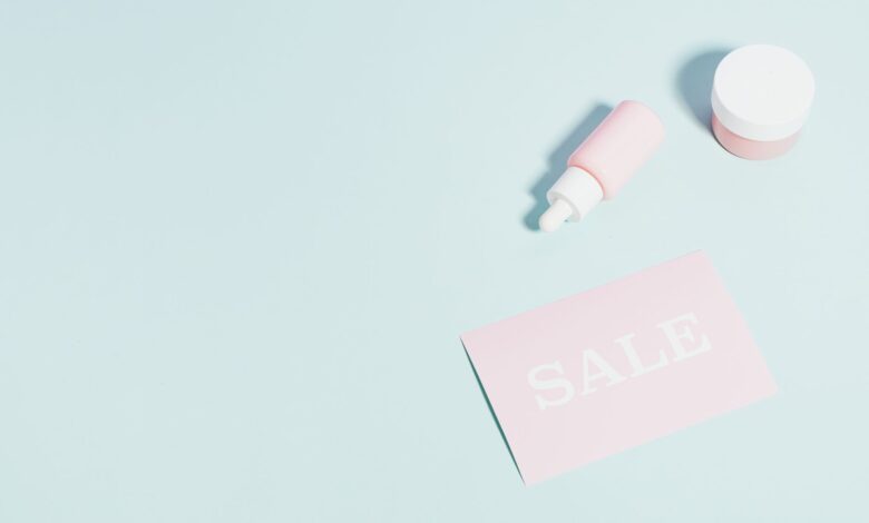 Pink beauty products and sale sign on pastel backdrop.
