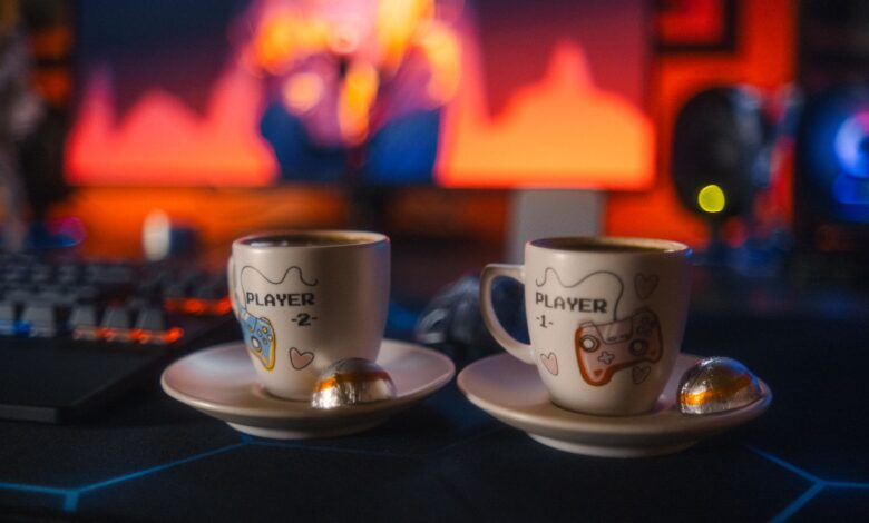Two gaming-themed espresso cups with chocolates on a colorful gaming setup background.