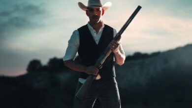 A cowboy in traditional attire holding a shotgun, standing outdoors in San Antonio, Texas.